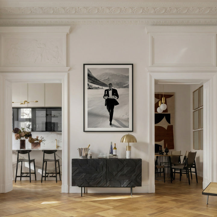 Modern interior with a black and white framed picture on a wall, a black sideboard, and a kitchen in the background.