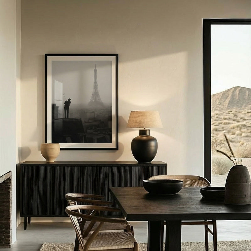 Modern dining room with dark wooden table and chairs, framed picture of Eiffel Tower, and lamp.